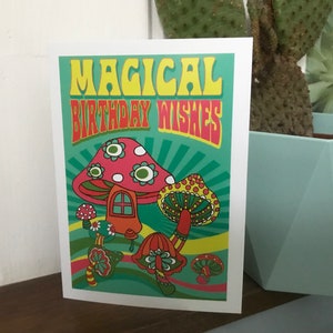 Op de afbeelding: Een kaart met een psychedelisch ontwerp met paddenstoelen en de tekst "Magical Birthday Wishes".