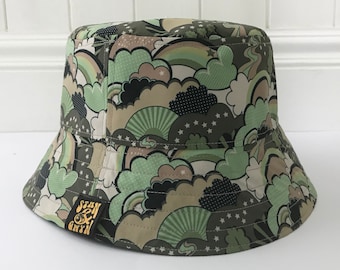 May include: A green bucket hat with a colorful print of clouds, rainbows, and stars. The hat has a black and white logo that says "Stan & Bryn" on the side.