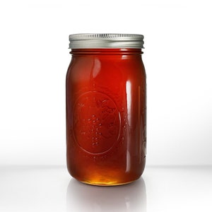 May include: A glass jar filled with honey. The jar has a silver lid and a textured design with a grape motif.