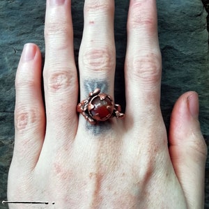 May include: A copper ring featuring a red carnelian stone set in a twisted wire design.