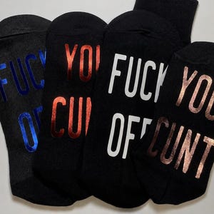 May include: Four black socks featuring the text "FUCK YOU OFF CUNT" printed in different metallic and matte colours. The first sock has blue metallic text, the second has red metallic text, the third has white matte text, and the fourth has rose gold metallic text.