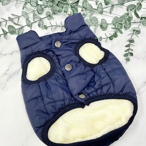 May include: A navy blue quilted dog vest with a white fleece lining. The vest has a zipper closure and two snap buttons.