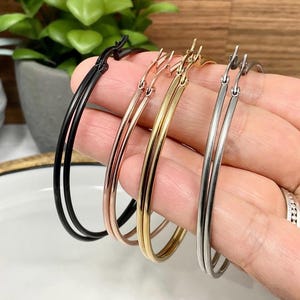 May include: A selection of hoop earrings in black, rose gold, gold, and silver. The earrings are displayed in a hand, highlighting their different metallic finishes. The hoops are simple and elegant, suitable for everyday wear.