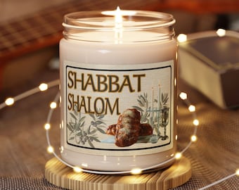 May include: A white candle with a brown label that says "Shabbat Shalom" and a picture of challah bread and a menorah. The candle is on a wooden coaster and surrounded by white fairy lights.