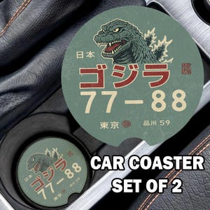 May include: Set of two car coasters featuring a vintage design with a Godzilla illustration. The coasters are green with red and white Japanese text and numbers. The text "CAR COASTER SET OF 2" is also visible.