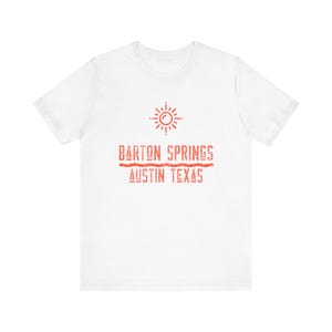 May include: White t-shirt with a red graphic design featuring a sun, the text "Barton Springs", and "Austin Texas".