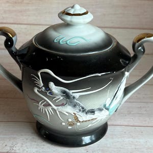 May include: A black and white porcelain teapot with a gold lid and handle. The teapot is decorated with a dragon design and has a blue and white floral pattern.