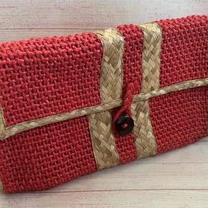 Può includere: Una pochette rossa intrecciata con chiusura a patta. La pochette presenta dettagli beige intrecciati e una chiusura con bottone scuro. La borsa è realizzata in un materiale intrecciato ed è progettata per essere un accessorio elegante.