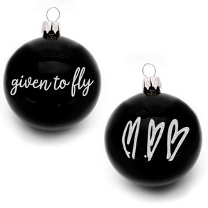 Op de afbeelding: Twee zwarte kerstballen met witte letters. Eén bal heeft de tekst "given to fly" en de andere bal heeft de letters "M.B." met twee harten.