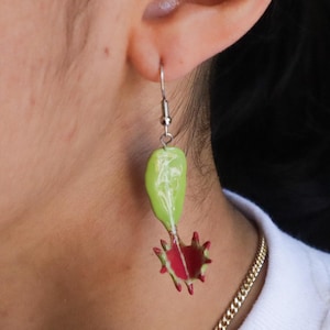 May include: A pair of dangle earrings featuring a green and red design. The earrings are shaped like a dragon fruit, with a green outer layer and a red inner layer.