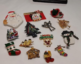 May include: A collection of fourteen Christmas-themed pins and brooches featuring various designs including a Santa Claus face, a snowman, a Christmas tree, a stocking, a nativity scene, an angel, and a Merry Christmas sign with colorful enamel.