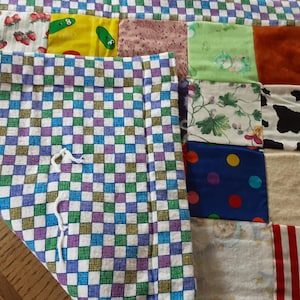 May include: A patchwork quilt with a checkered border. The quilt is made of various fabrics with different patterns, including polka dots, stripes, and floral designs. The quilt is a great way to add a touch of handmade charm to any room.