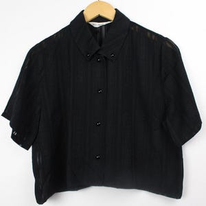 May include: A black short-sleeved button-down shirt with a striped pattern. The shirt has a collared neckline and a cropped hem.