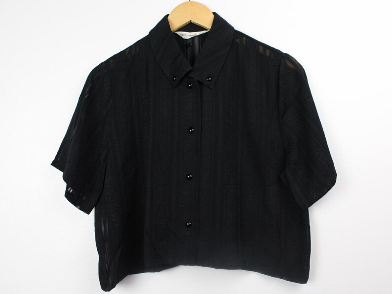 May include: A black short-sleeved button-down shirt with a striped pattern. The shirt has a collared neckline and a cropped hem.