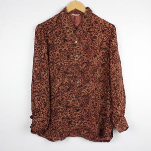 May include: A long-sleeved button-down shirt featuring a dense, intricate pattern in shades of dark red, brown, and black. The shirt has a standard collar, a front button placket with visible buttons, and cuffs at the ends of the long sleeves.