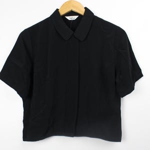 May include: A black short-sleeved collared shirt with a pleated front.