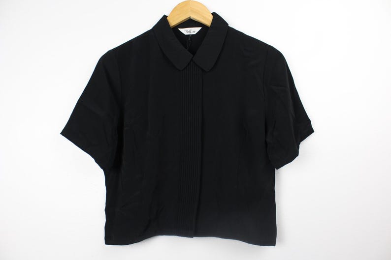 May include: A black short-sleeved collared shirt with a pleated front.