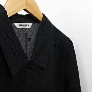 May include: A black textured collared shirt with a V-neck and a label that reads "NARUDAN".