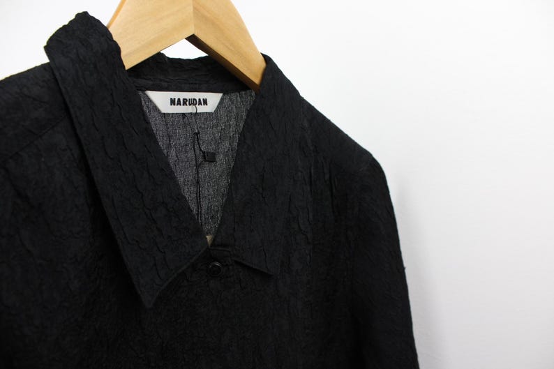 May include: A black textured collared shirt with a V-neck and a label that reads "NARUDAN".