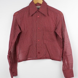 May include: A long-sleeve button-down shirt in a deep red color featuring a repeating white polka dot pattern. The shirt has a pointed collar, a single chest pocket on the left side, and matching red buttons down the front placket and on the cuffs.