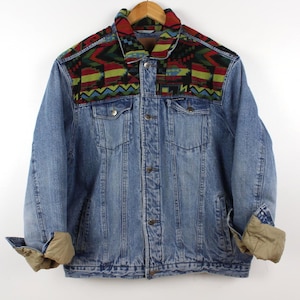 May include: A light blue denim jacket with a colorful patterned collar and yoke. The jacket has a button-up front, two chest pockets, and rolled-up sleeves. The collar features a geometric design in red, green, black, and blue.
