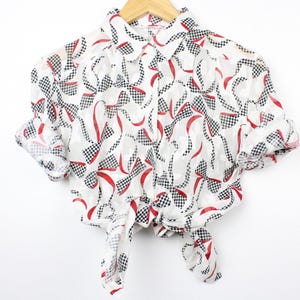 May include: White sheer button-up shirt with a red and black geometric pattern. The shirt has a collar and short sleeves and is tied at the front.