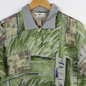 Puede incluir: Una camisa polo de manga corta con cuello abotonado y estampado verde, azul y blanco. La camisa tiene un aspecto descolorido y vintage.