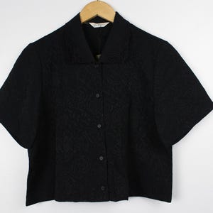 May include: A black short-sleeved button-down shirt with a floral pattern. The shirt has a collar and a button-up front.