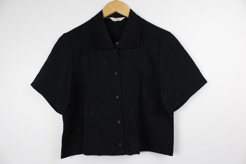 May include: A black short-sleeved button-down shirt with a floral pattern. The shirt has a collar and a button-up front.
