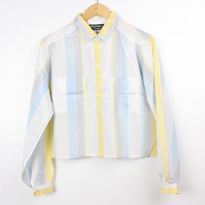 Puede incluir: Una camisa de manga larga con botones y un patrón a rayas en amarillo, azul y blanco.