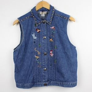 May include: A blue denim vest featuring a collar adorned with silver-toned metal studs. The front displays vertical pleats and various embroidered motifs including cowboy boots, cacti, and a lasso. It has a button-down front with metal buttons.