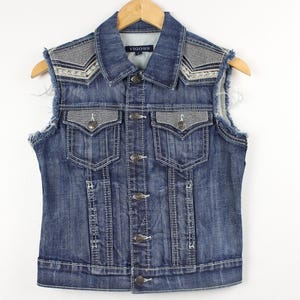 May include: A blue denim vest with a frayed hem and embroidered details on the shoulders. The vest has a button closure and two front pockets.