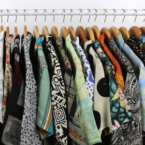 May include: A rack of colorful patterned shirts hanging on wooden hangers. The shirts are all different colors and patterns, and some have a floral design.
