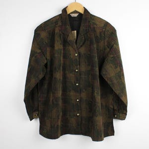 Puede incluir: Una camisa de manga larga con botones en un patrón de cuadros de color verde oliva oscuro y marrón. La camisa presenta un cuello con solapas, una tapeta frontal con botones a juego y puños abotonados en las mangas.