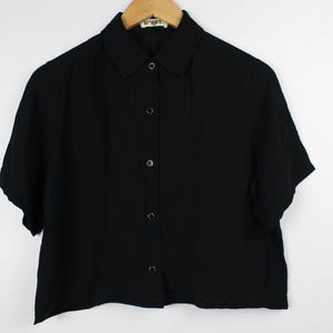 May include: A black short-sleeved button-down shirt with a collared neckline. The shirt has a slightly cropped length and a textured fabric.