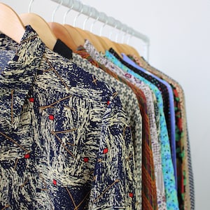 May include: A collection of patterned shirts hanging on hangers. The shirts are in various colors and patterns, including blue, red, green, and yellow. The shirts are all made of a lightweight fabric and have a relaxed fit.