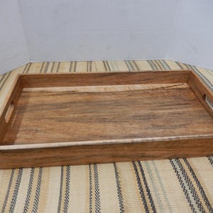 May include: A rectangular wooden serving tray with a natural wood grain finish. The tray has a raised edge and cut-out handles on each end. The tray is approximately 51 cm long and 30 cm wide.