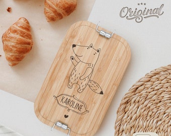 May include: A wooden lunchbox with a fox design and the name "KAROLINE" engraved on it. The lunchbox has two silver clasps and is made of natural bamboo.