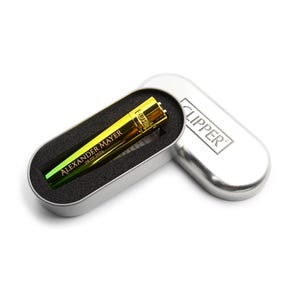 May include: A gold and green gradient Clipper lighter with the name "Alexander Mayer" and the date "29.02.2024" printed on it. The lighter is in a silver metal case with the word "CLIPPER" printed on the lid.