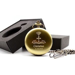 Puede incluir: Un reloj de bolsillo dorado con cadena, sobre un fondo blanco. La esfera del reloj presenta una cruz, un libro abierto y el nombre "Christian" con la fecha "01.05.2025". Una caja negra está abierta detrás del reloj.