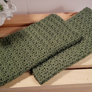 May include: Two green crocheted dishcloths, folded and stacked on a wooden crate.