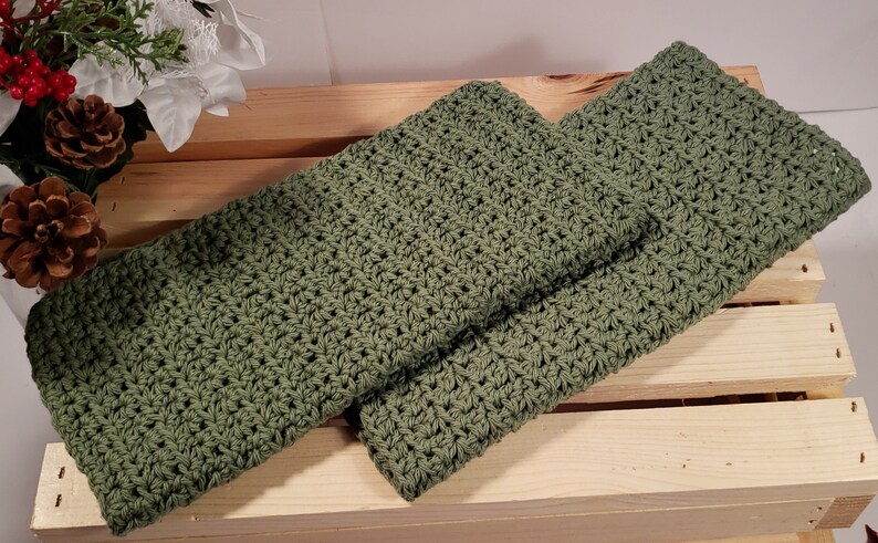 May include: Two green crocheted dishcloths, folded and stacked on a wooden crate.