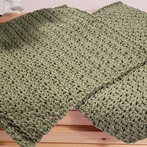 May include: Two green crocheted dishcloths, folded and stacked on top of each other, on a wooden surface.