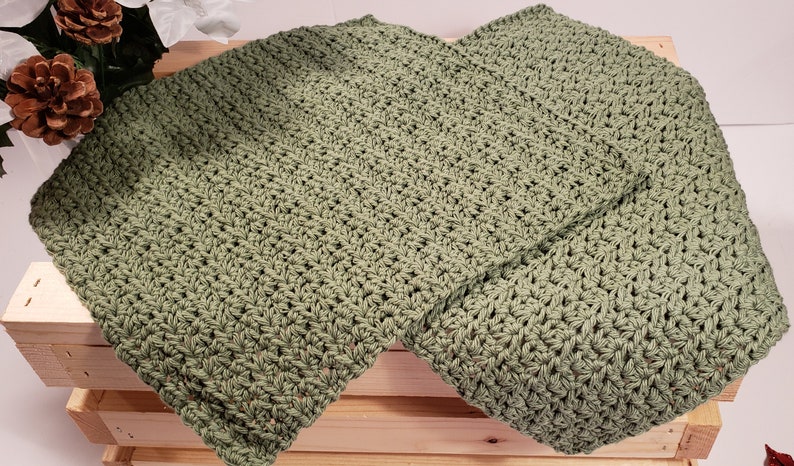 May include: Two green crocheted dishcloths, folded and stacked on top of each other, on a wooden surface.