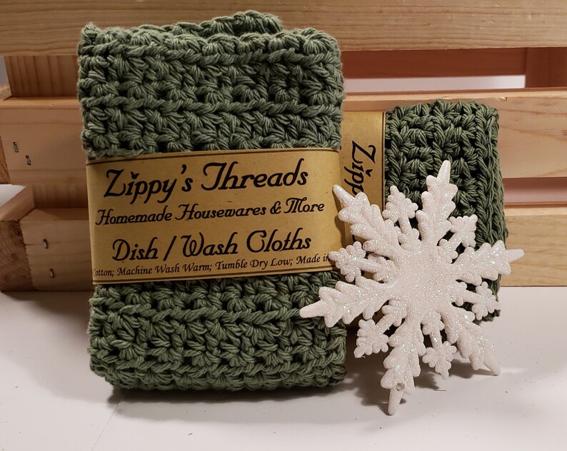 May include: Two green crocheted dishcloths with a white snowflake ornament. The dishcloths are labeled "Zippy's Threads Homemade Housewares & More Dish/Wash Cloths".