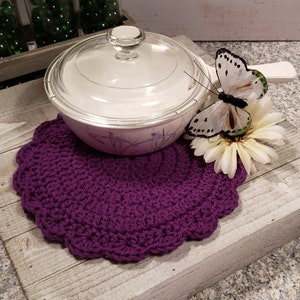 May include: Purple crocheted pot holder with a white ceramic pot with a glass lid on top. A white butterfly with black markings is perched on a white flower.