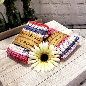 Pu&ograve; includere: Due strofinacci in crochet a righe rosa, bianco e grigio con un'etichetta marrone che recita "ippy's Threads Handmade Housewares & More Dish/Wash Cloths".