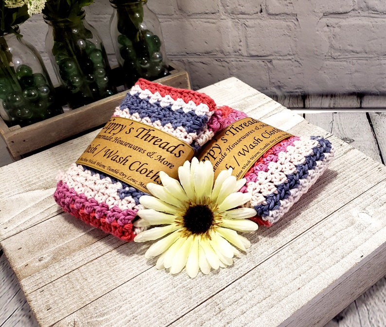 Pu&ograve; includere: Due strofinacci in crochet a righe rosa, bianco e grigio con un'etichetta marrone che recita "ippy's Threads Handmade Housewares & More Dish/Wash Cloths".