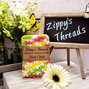 May include: A colourful crocheted washcloth with a label that reads "Zippy's Threads Homemade Housewares & More Wash Cloths".