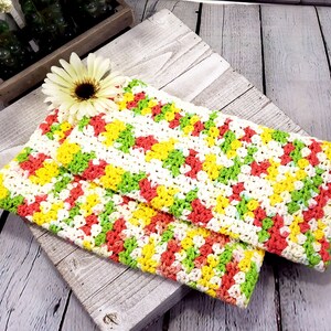 May include: Two crocheted dishcloths in a chevron pattern with yellow, green, white and pink yarn.